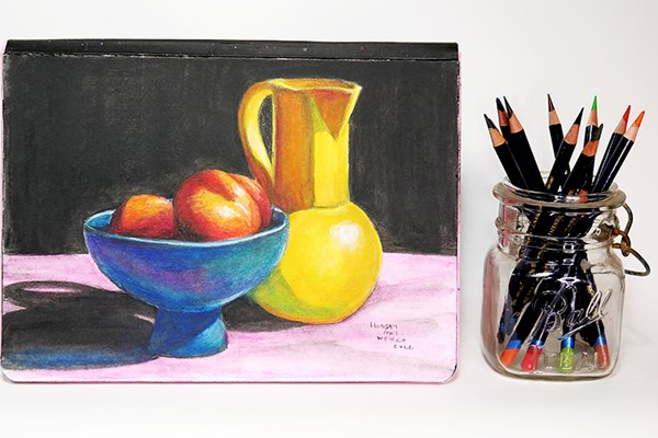 Still life drawing of fruit and pitcher next to Inktense pencils in a mason jar