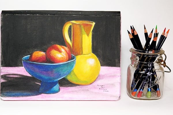 Still life drawing of fruit and pitcher next to Inktense pencils in a mason jar